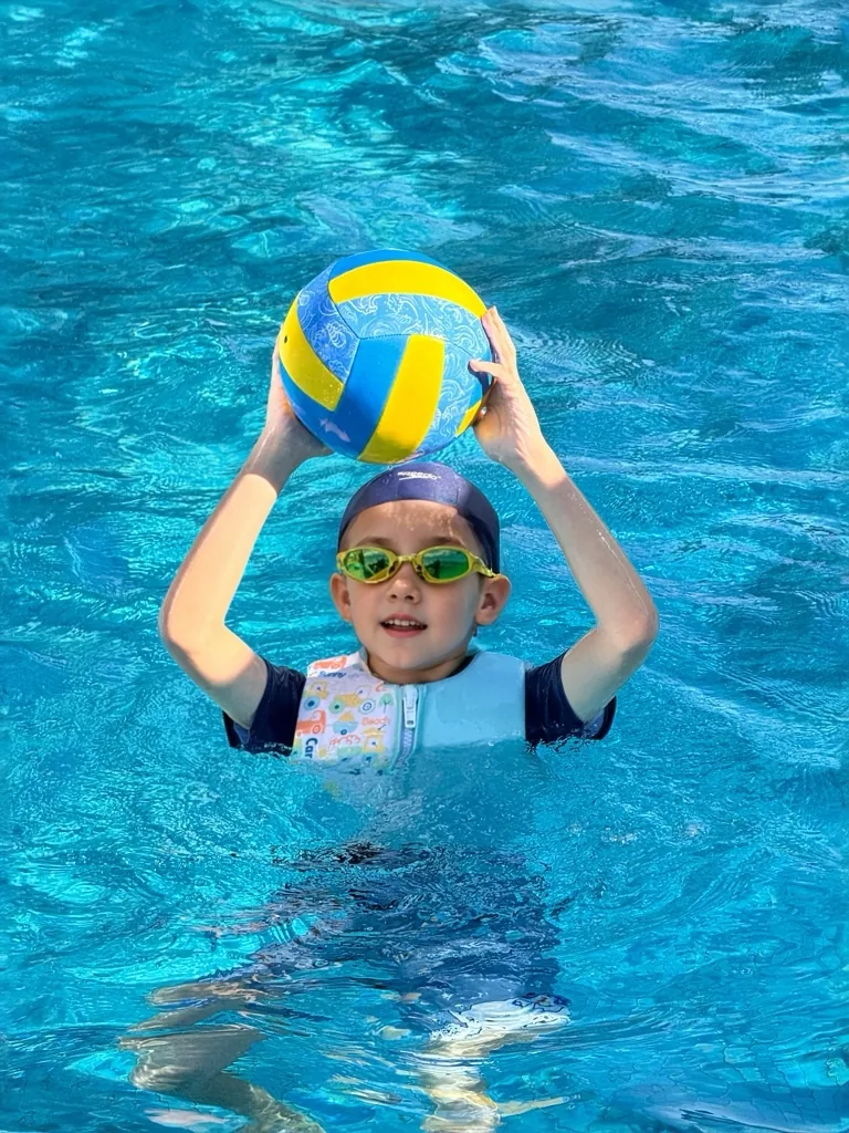 Child holding a neoprene beach volleyball in a swimming pool